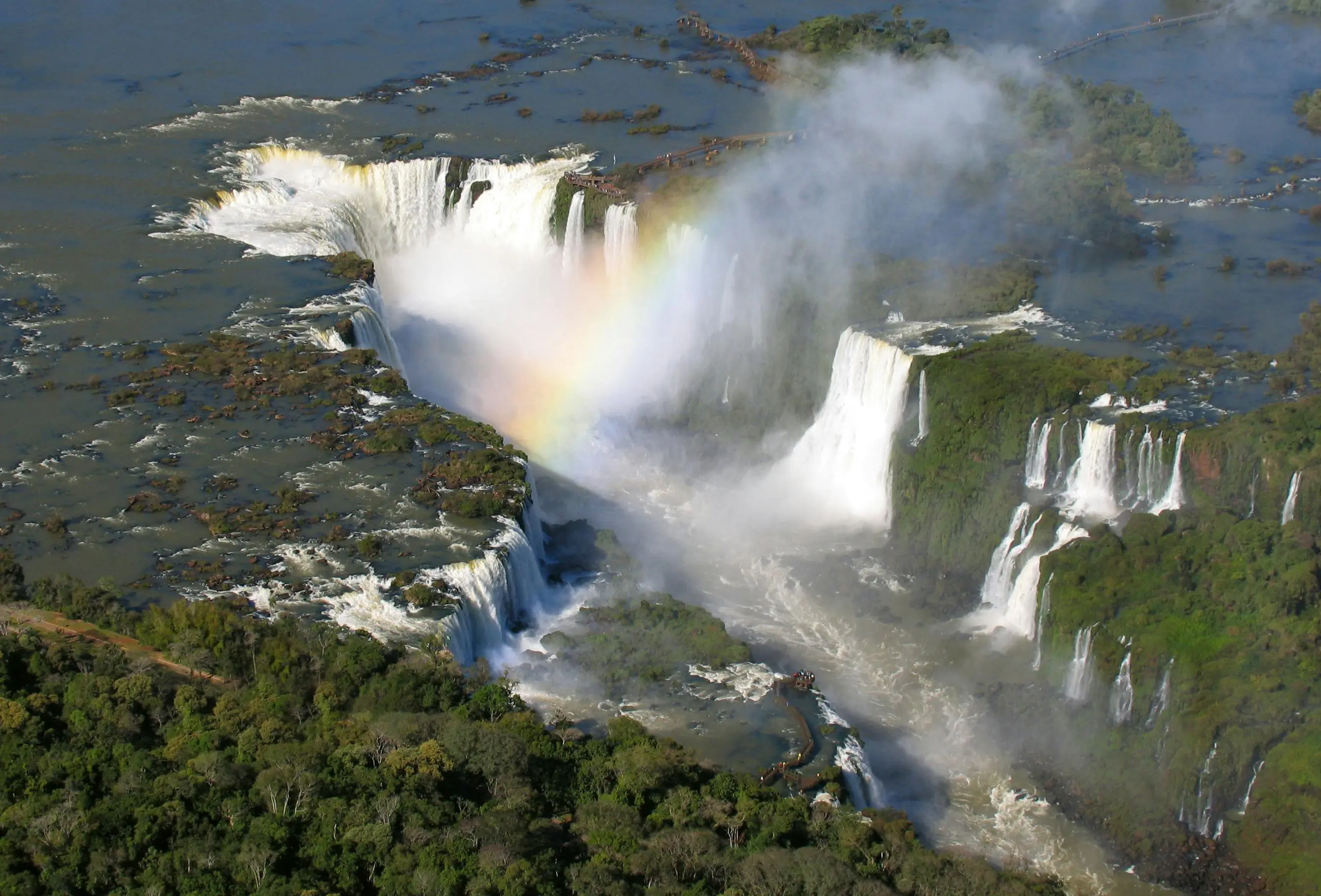 Aerial view of the Iguazu Falls, showcasing multiple cascading waterfalls surrounded by lush green vegetation.