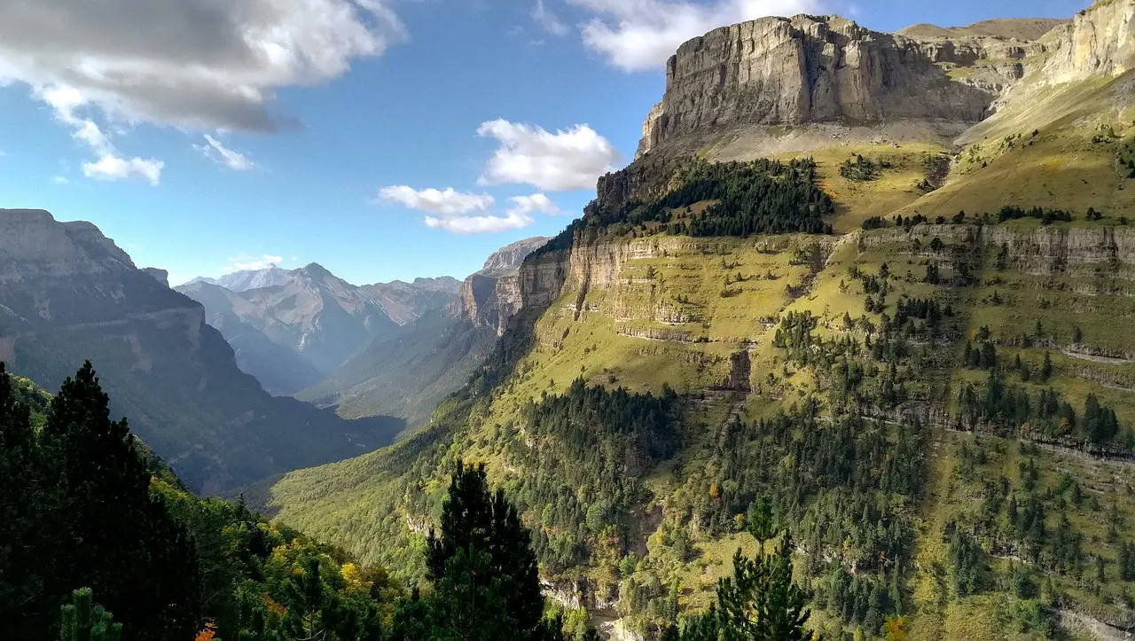 Rolling hills and a winding path through Ordesa y Monte Perdido National Park, surrounded by lush greenery and dramatic mountain scenery.