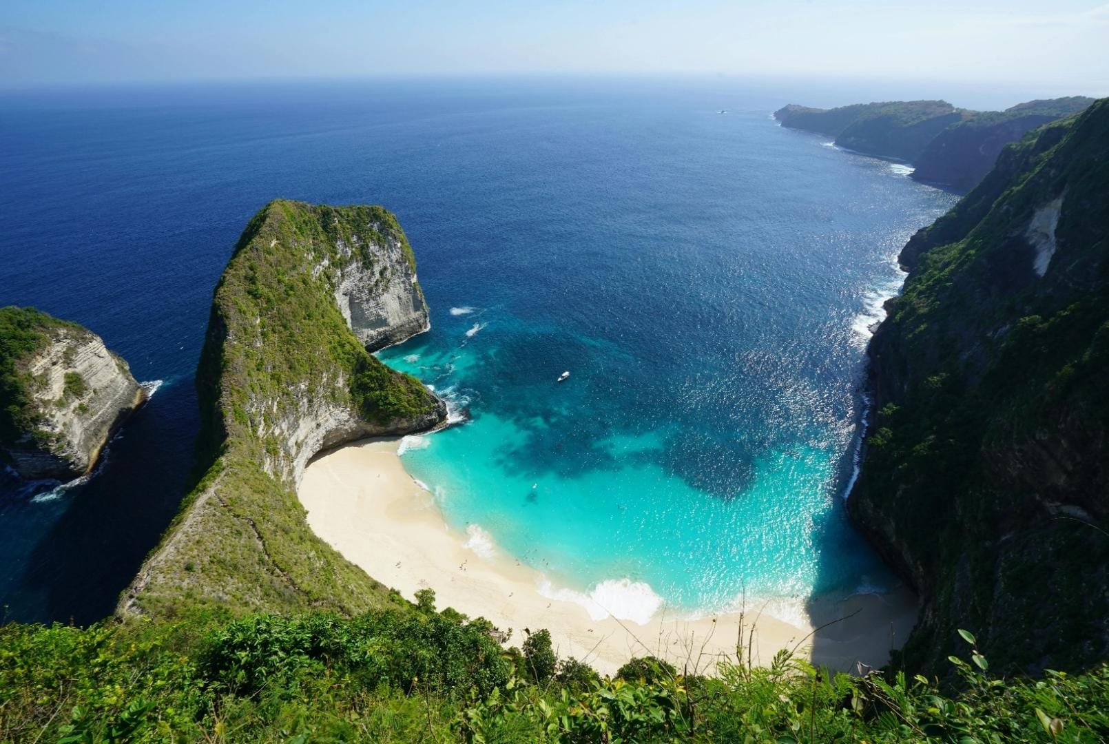 Stunning coastline in Indonesia featuring a small beach with white sand, crystal-clear waters, and lush greenery surrounding the area.