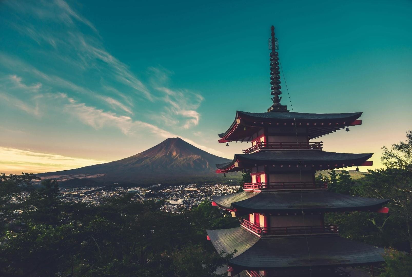 Japanese tower overlooking a village at the foot of Mount Fuji during sunset, with the mountain and sky bathed in warm colors.