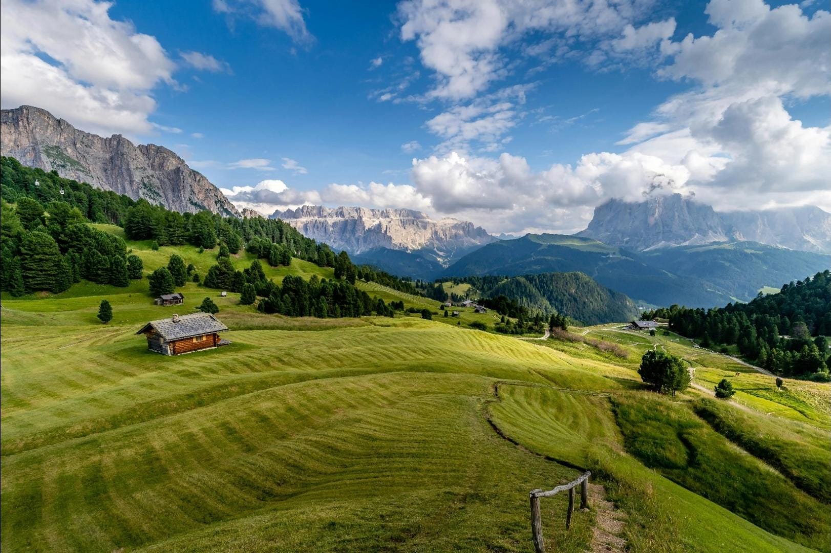 A meadow in the Lauterbrunnental valley in Switzerland, with a small cabin, surrounded by trees and towering mountains.